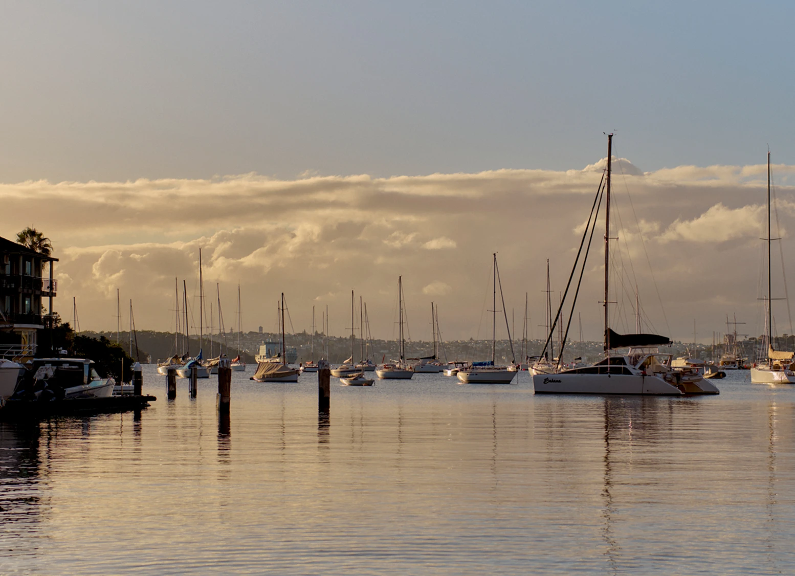 Sailboats settle into the harbour as the sun sets across
                                            Kirribilli